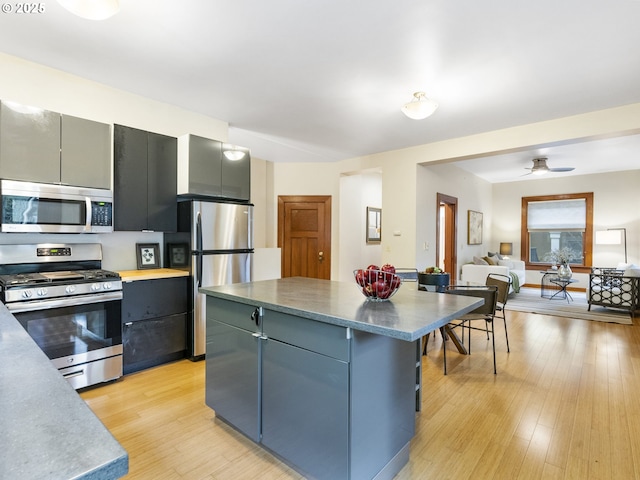 kitchen with stainless steel appliances, a kitchen island, open floor plan, light wood-type flooring, and gray cabinets