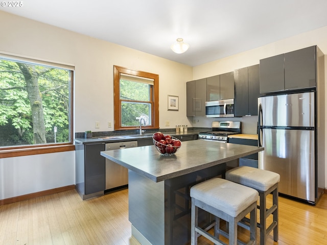 kitchen featuring a breakfast bar area, stainless steel appliances, dark countertops, a sink, and light wood-type flooring