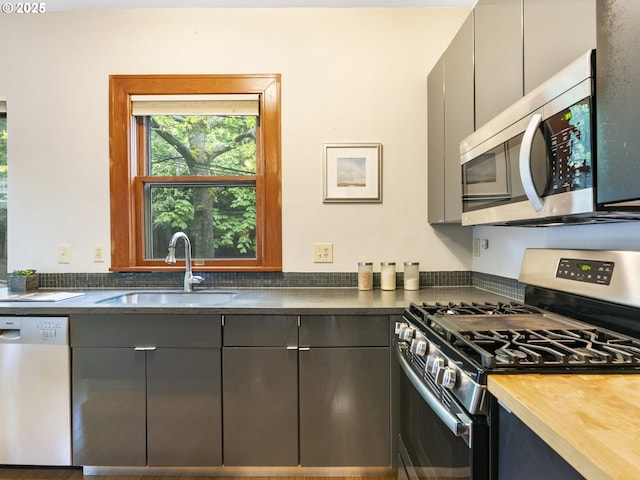 kitchen with stainless steel appliances, butcher block countertops, a sink, and gray cabinetry