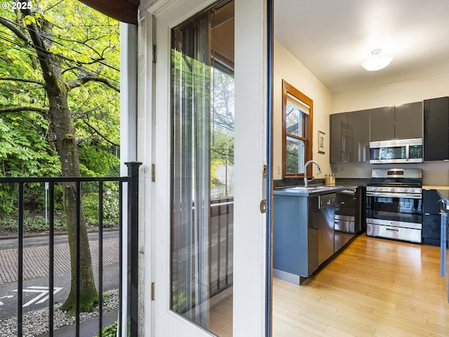 kitchen with stainless steel appliances, a sink, light wood finished floors, dark countertops, and modern cabinets