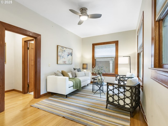 living area featuring baseboards, ceiling fan, and light wood finished floors