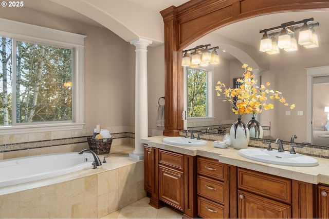 bathroom featuring vanity, tiled tub, decorative columns, and a healthy amount of sunlight