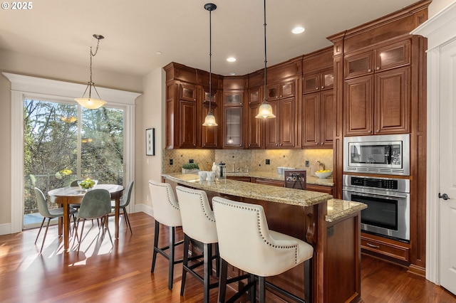 kitchen with light stone counters, decorative light fixtures, appliances with stainless steel finishes, dark hardwood / wood-style flooring, and a kitchen island