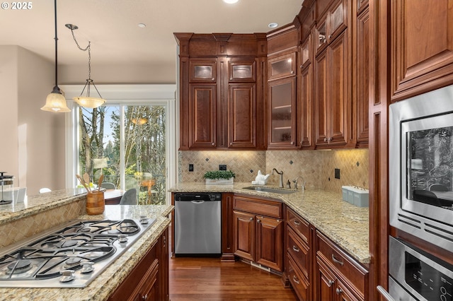 kitchen featuring sink, hanging light fixtures, stainless steel appliances, light stone countertops, and backsplash