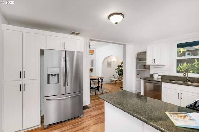 1225 N Emerson St, Portland, OR 97217 - kitchen with appliances with stainless steel finishes, arched walkways, white cabinets, light wood-style floors, and dark stone countertops