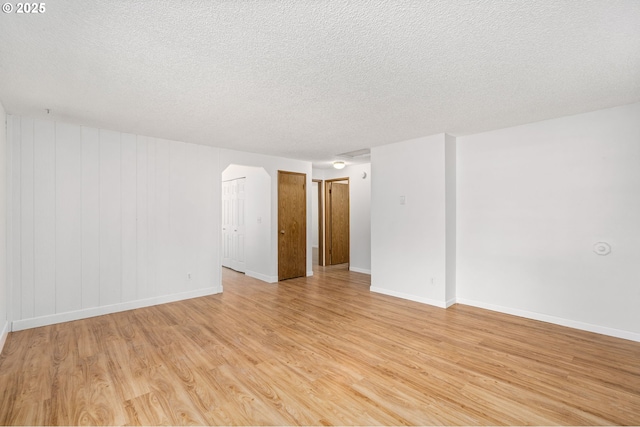 6654 SW Capitol Hwy, Portland, OR 97219 - empty room with light wood-type flooring, a textured ceiling, baseboards, and arched walkways