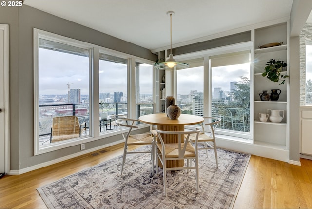 dining room with baseboards, light wood-style floors, a city view, and a healthy amount of sunlight