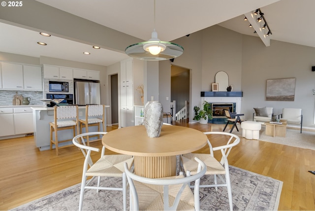 dining space with a glass covered fireplace, vaulted ceiling, recessed lighting, and light wood-type flooring