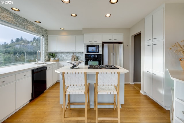 kitchen with white cabinetry, black appliances, light wood finished floors, and a sink