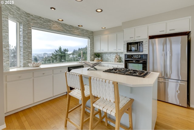 kitchen featuring light wood finished floors, decorative backsplash, black appliances, light countertops, and a kitchen bar