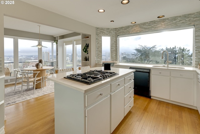 kitchen featuring black appliances, light wood-style flooring, a sink, a kitchen island, and white cabinets