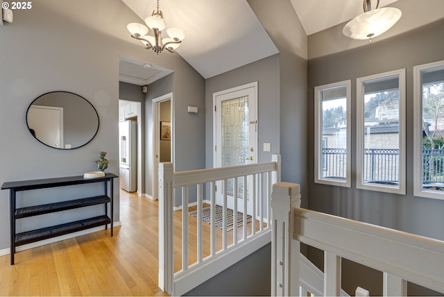 hallway with baseboards, an inviting chandelier, vaulted ceiling, light wood-style floors, and an upstairs landing