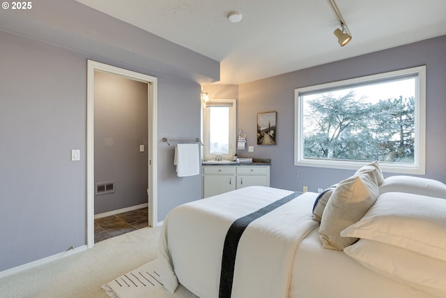 bedroom with track lighting, visible vents, baseboards, light colored carpet, and vaulted ceiling