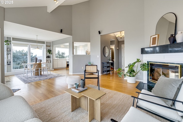 living room with light wood-type flooring, a fireplace with flush hearth, a notable chandelier, beam ceiling, and baseboards