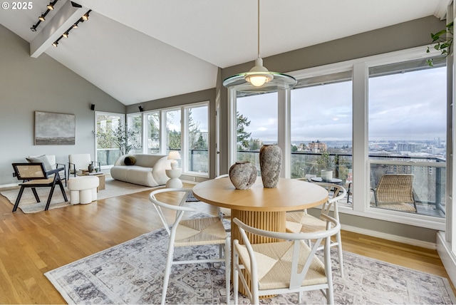 dining room featuring rail lighting, baseboards, light wood-type flooring, and high vaulted ceiling