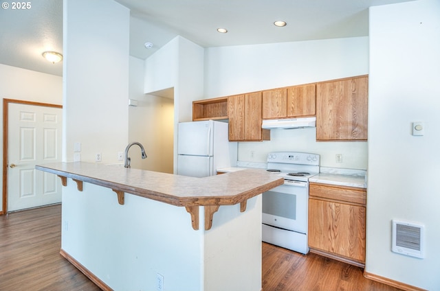 kitchen with sink, dark hardwood / wood-style floors, a kitchen breakfast bar, kitchen peninsula, and white appliances