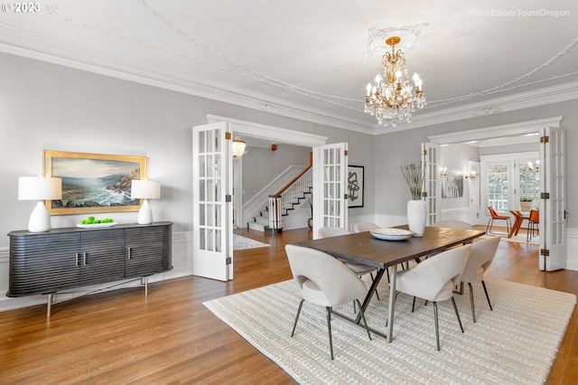 dining space with ornamental molding, an inviting chandelier, french doors, and hardwood / wood-style flooring