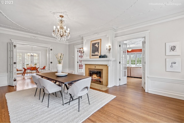 dining room featuring a tiled fireplace, a notable chandelier, hardwood / wood-style floors, and crown molding