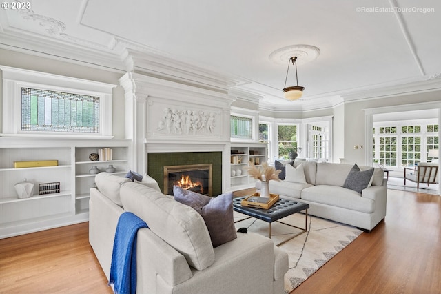 living room with a tiled fireplace, light hardwood / wood-style flooring, crown molding, and built in shelves