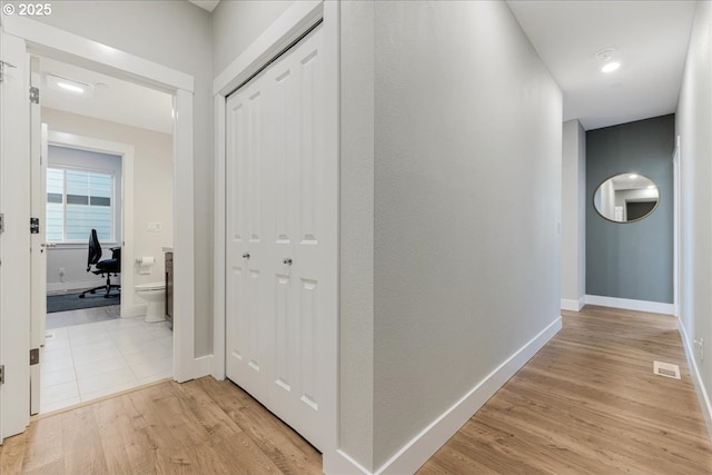 hall featuring visible vents, light wood-style flooring, and baseboards