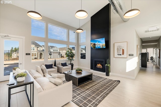 living room featuring a towering ceiling, a fireplace, baseboards, and wood finished floors