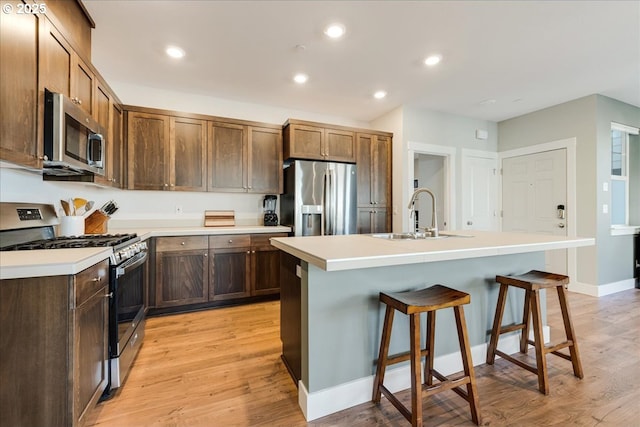 kitchen with stainless steel appliances, light wood-style floors, a sink, and a kitchen breakfast bar