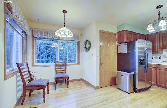 kitchen with a notable chandelier, light wood-style flooring, stainless steel fridge with ice dispenser, decorative backsplash, and hanging light fixtures