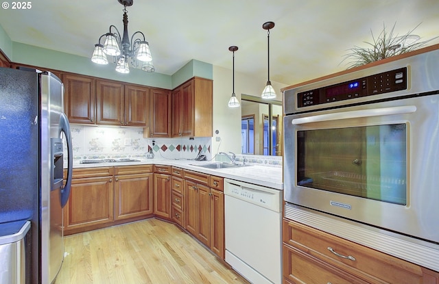 kitchen featuring a sink, light countertops, appliances with stainless steel finishes, pendant lighting, and light wood-type flooring