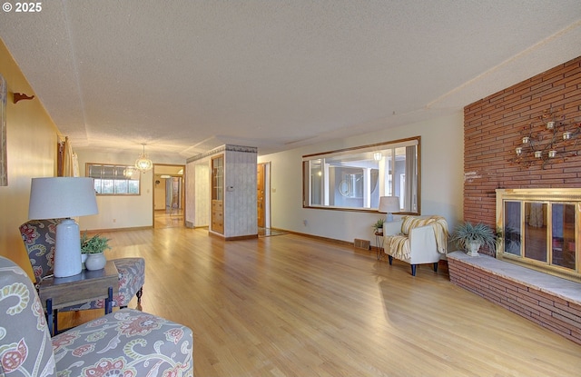 living area with visible vents, light wood-style flooring, a textured ceiling, a fireplace, and baseboards