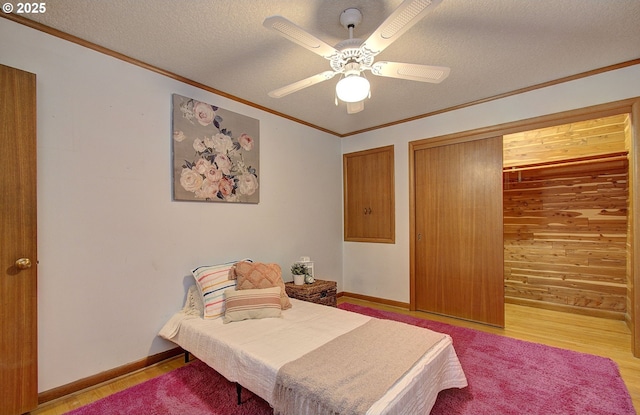 bedroom with baseboards, ceiling fan, a textured ceiling, crown molding, and light wood-type flooring