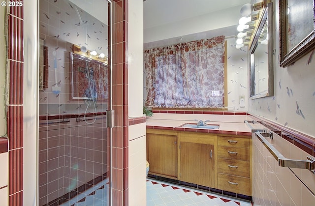 full bath with a wainscoted wall, a stall shower, tile walls, wallpapered walls, and vanity