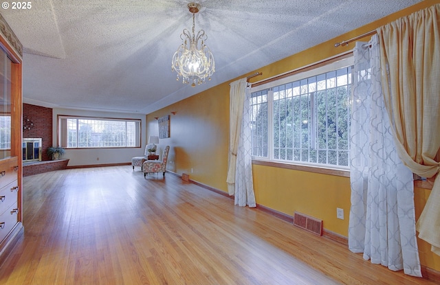 unfurnished room with visible vents, a brick fireplace, a chandelier, wood finished floors, and a textured ceiling