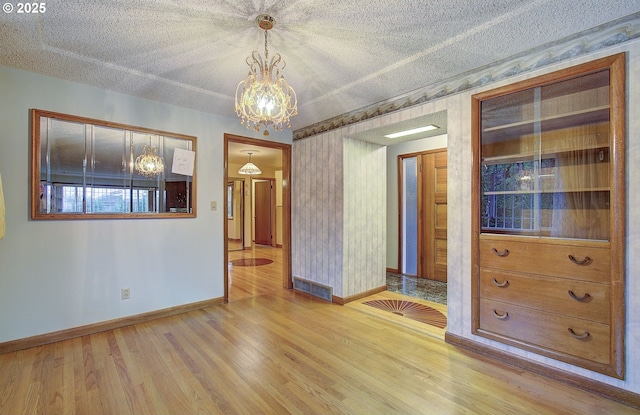 empty room featuring visible vents, baseboards, a textured ceiling, and wood finished floors