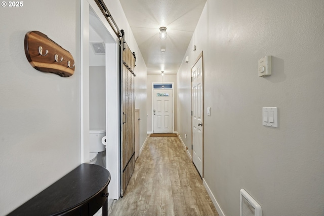 hall featuring light wood-type flooring, a barn door, visible vents, and baseboards