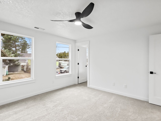 spare room featuring light carpet, baseboards, visible vents, a ceiling fan, and a textured ceiling