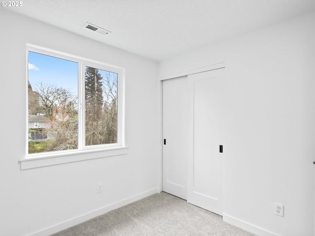 unfurnished bedroom featuring light carpet, multiple windows, visible vents, and baseboards