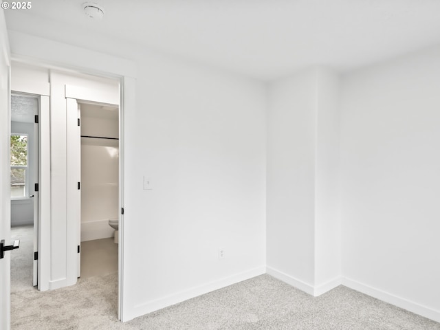 unfurnished bedroom with light carpet, a spacious closet, and baseboards