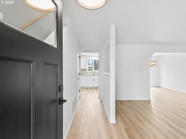 hall with an inviting chandelier, light wood-style flooring, visible vents, and baseboards