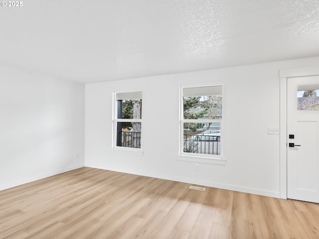 empty room with baseboards, visible vents, light wood-style flooring, and a textured ceiling