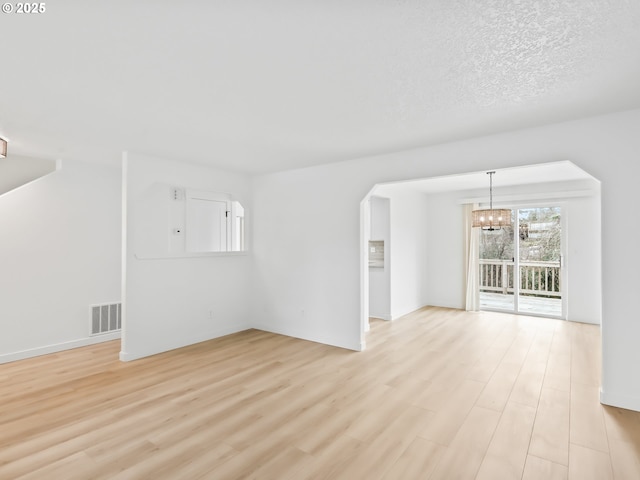 unfurnished living room with a textured ceiling, light wood-type flooring, visible vents, and an inviting chandelier