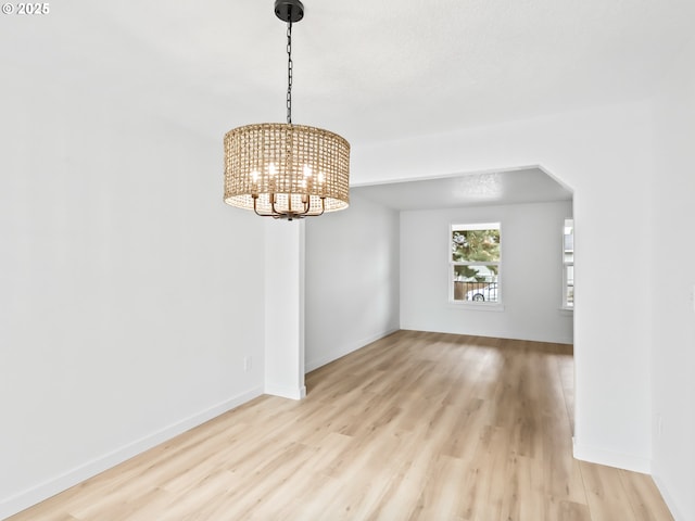 unfurnished room with arched walkways, a notable chandelier, light wood-style flooring, and baseboards