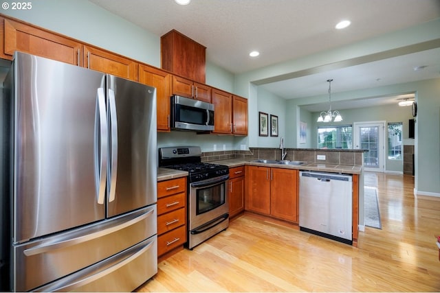 kitchen featuring stainless steel appliances, a peninsula, a sink, brown cabinetry, and recessed lighting