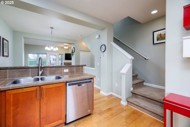 kitchen featuring stainless steel dishwasher, a sink, brown cabinetry, light wood finished floors, and a chandelier