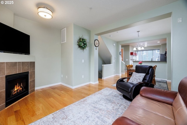 living area with wood finished floors, a tiled fireplace, a chandelier, stairway, and baseboards