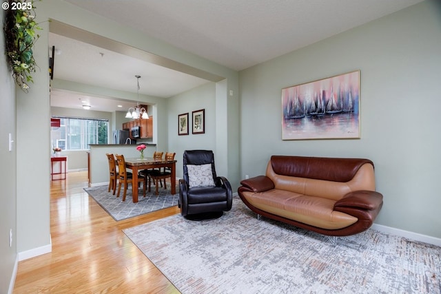 living room with light wood-style floors, a chandelier, and baseboards