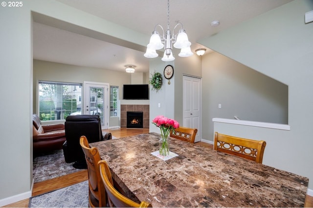 dining area featuring a chandelier, light wood finished floors, baseboards, and a tiled fireplace