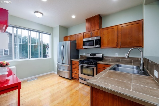 kitchen with appliances with stainless steel finishes, a sink, brown cabinets, light wood-style floors, and recessed lighting