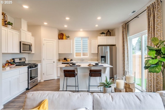 kitchen featuring wood-type flooring, stainless steel appliances, a breakfast bar, white cabinetry, and a kitchen island with sink