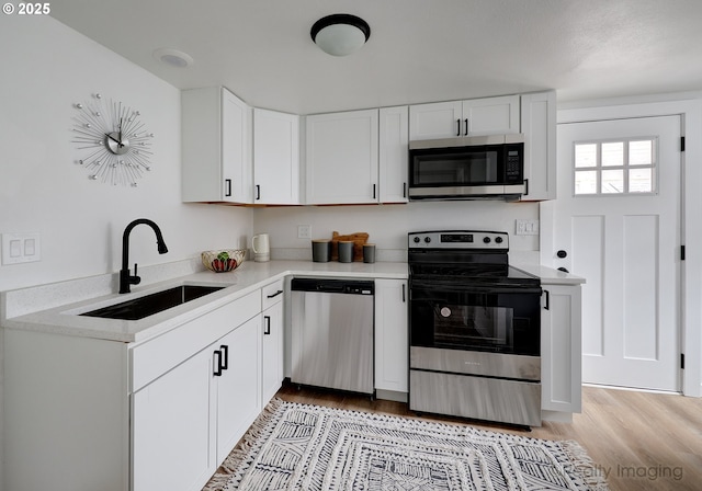 kitchen featuring appliances with stainless steel finishes, a sink, light countertops, and light wood finished floors