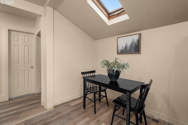 dining room featuring wood-type flooring and lofted ceiling with skylight